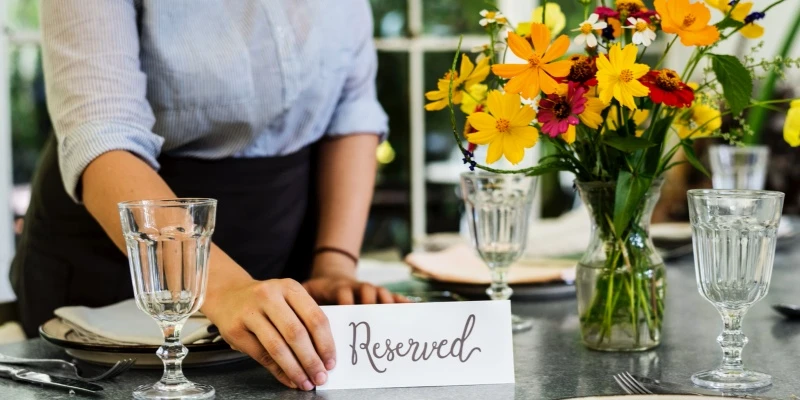 一位服務員，將字卡放在花瓶旁，表示此餐桌已訂位。